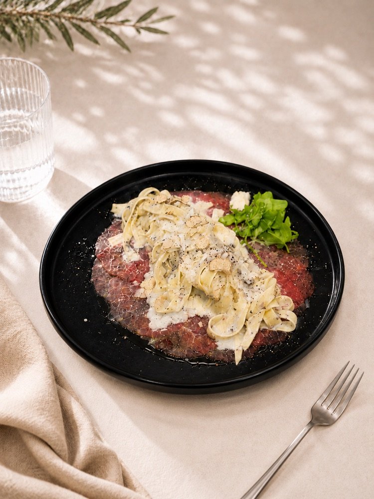 Tagliolini in Trüffelsoße mit gehobeltem Trüffel auf einem Spiegel aus rohem Rindercarpaccio