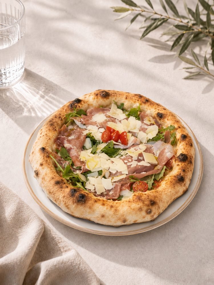 Pizza mit Fior di Latte, rohem Parmaschinken, frischem Rucola, Cherrytomaten und Grana-Scheiben